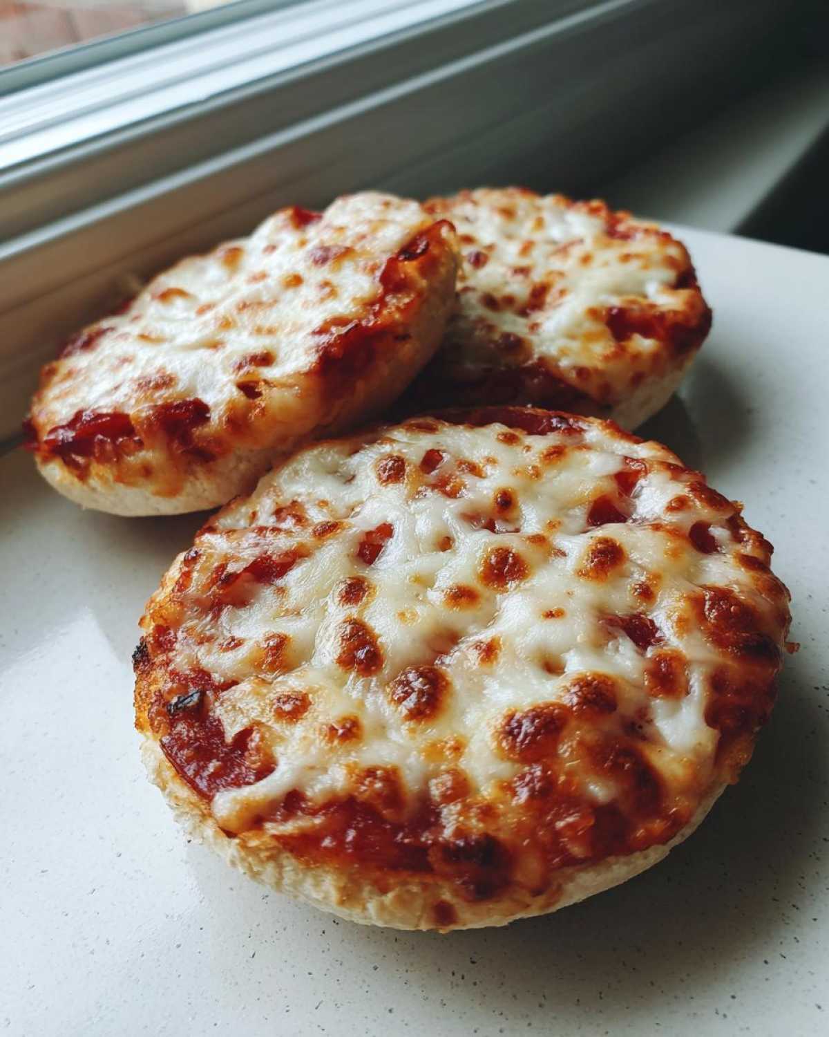 Three perfectly baked english muffin pizza halves topped with melted, bubbly cheese and tomato sauce.