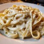 Close-up of fettuccine pasta coated in rich homemade alfredo sauce and topped with cracked black pepper.