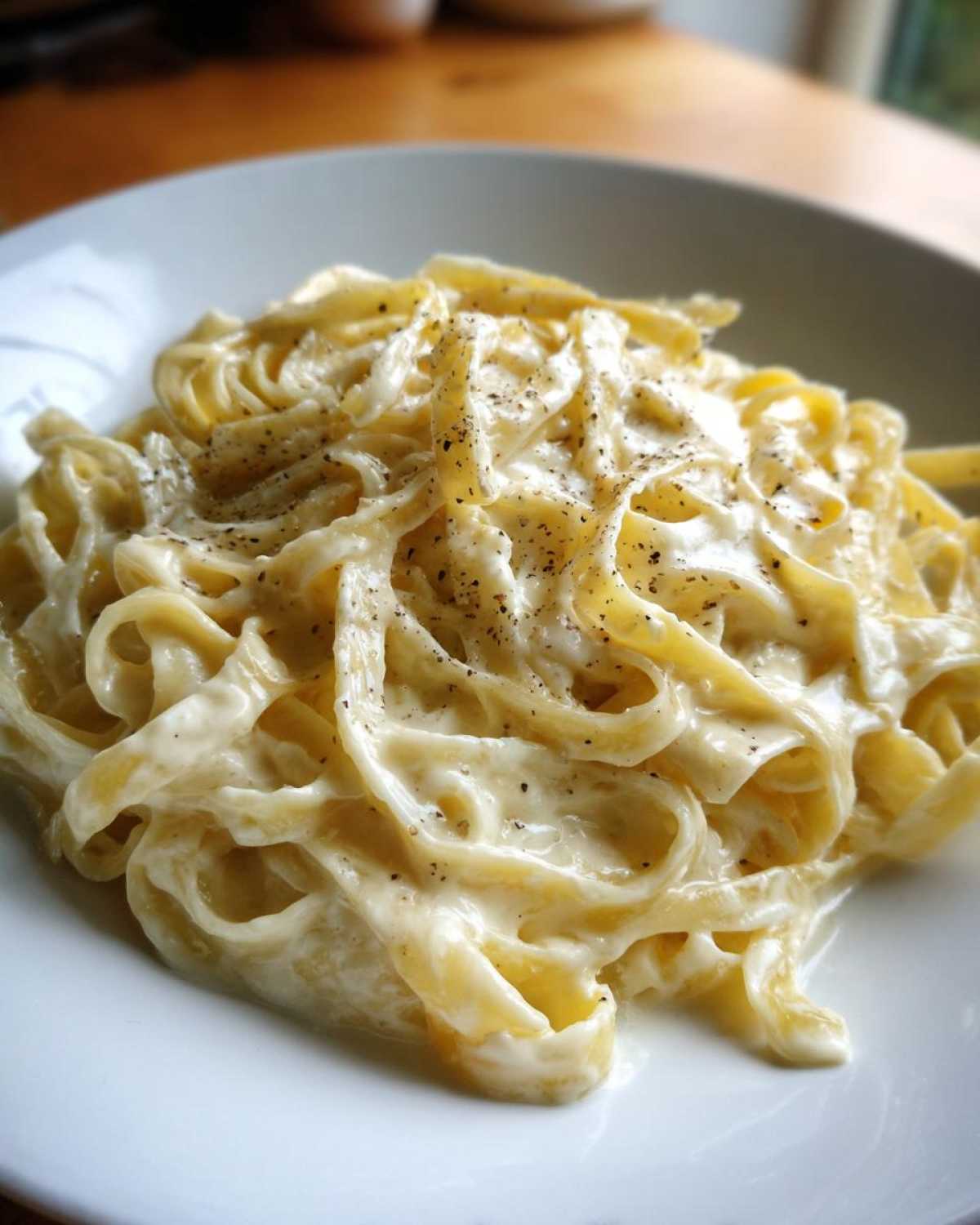 Close-up of fettuccine pasta coated in creamy homemade alfredo sauce and topped with black pepper.