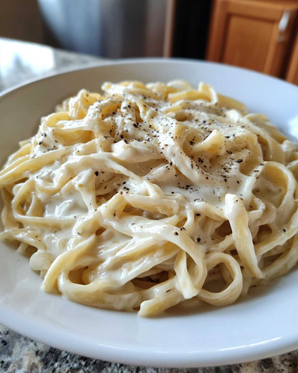 Close-up of fettuccine pasta generously coated in creamy homemade alfredo sauce and topped with cracked black pepper.
