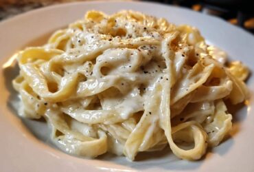 Close-up of fettuccine pasta coated in rich homemade alfredo sauce and topped with cracked black pepper.