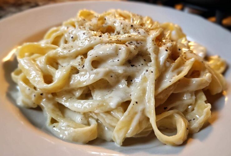 Close-up of fettuccine pasta coated in rich homemade alfredo sauce and topped with cracked black pepper.