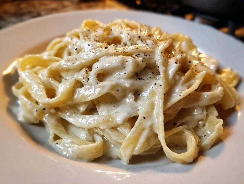 Close-up of fettuccine pasta coated in rich homemade alfredo sauce and topped with cracked black pepper.