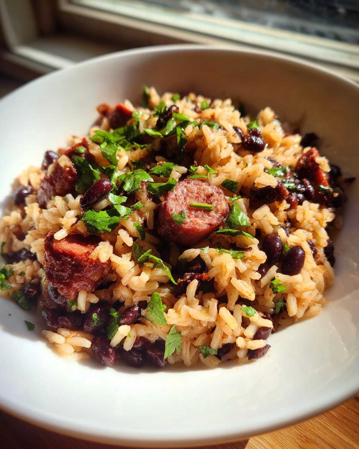 Close-up of savory black beans and rice mixed with sliced sausage and topped with fresh parsley.