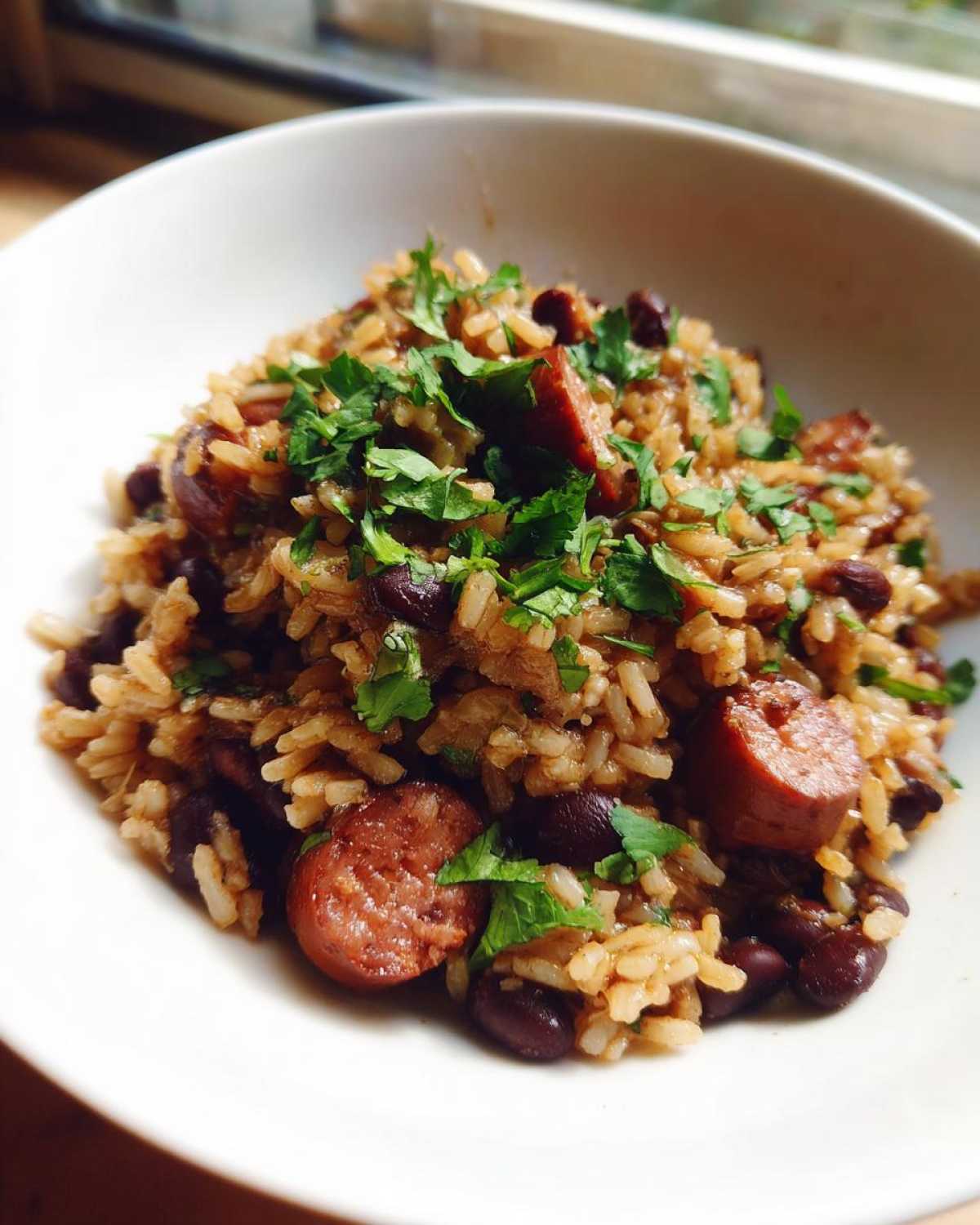 Close-up of a serving of flavor-packed black beans and rice mixed with sliced sausage and topped with fresh parsley.