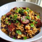 Close-up of savory black beans and rice mixed with sliced sausage and topped with fresh parsley.