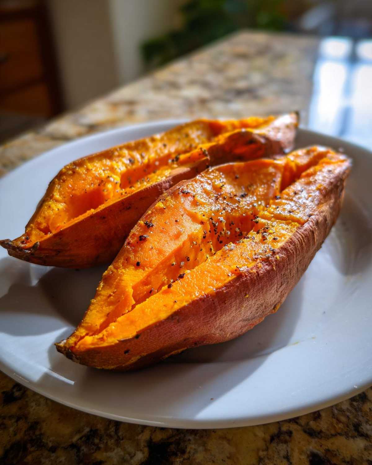Two halves of a fluffy baked sweet potato seasoned with salt and pepper on a white plate.
