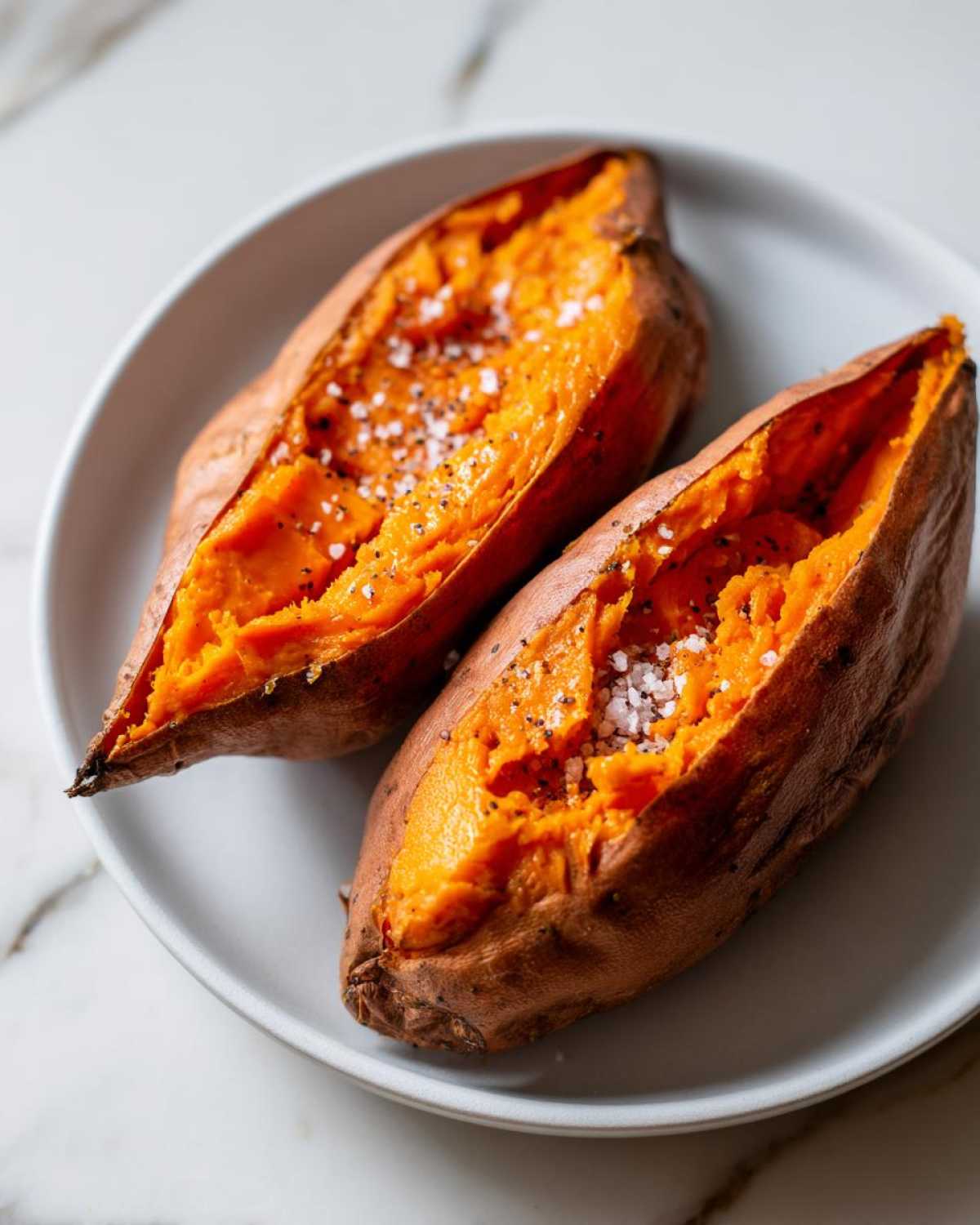 Two halves of a fluffy baked sweet potato topped with coarse sea salt and black pepper.