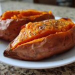 Close-up of a fluffy baked sweet potato, split open and seasoned with coarse salt and black pepper.