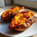 Two fluffy baked sweet potatoes, split open and seasoned, sitting on a white plate.