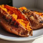 Two perfectly baked sweet potatoes split open showing fluffy orange interior.