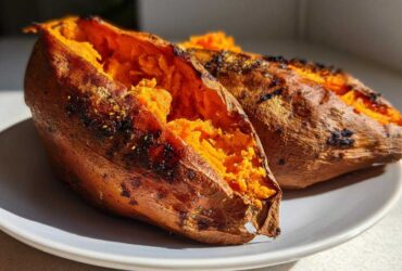 Two perfectly baked sweet potatoes split open showing fluffy orange interior.