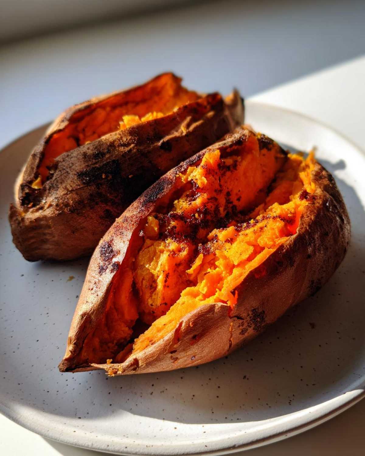 Two fluffy baked sweet potatoes split open on a plate, showing bright orange flesh.