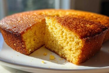 A close-up of a slice cut from a round buttermilk cornbread, showing its fluffy yellow interior and golden-brown crust.