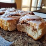 Close-up of a fluffy cinnamon roll broken open, showing the soft interior and thick white icing.