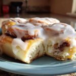Close-up of a fluffy cinnamon roll topped with thick, white icing, sitting on a blue plate.