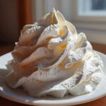 Close-up of a perfectly piped swirl of white, fluffy cream cheese frosting on a small white plate.