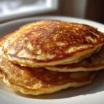 A close-up stack of three fluffy greek yogurt pancakes with golden-brown, perfectly cooked tops.