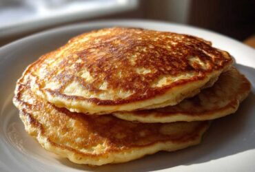 A close-up stack of three fluffy greek yogurt pancakes with golden-brown, perfectly cooked tops.