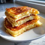 A close-up stack of three incredibly fluffy pancakes drizzled with syrup, showcasing their airy interior.