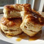 Close-up of fluffy sweet potato biscuits stacked on a white plate, drizzled with a shiny glaze or syrup.