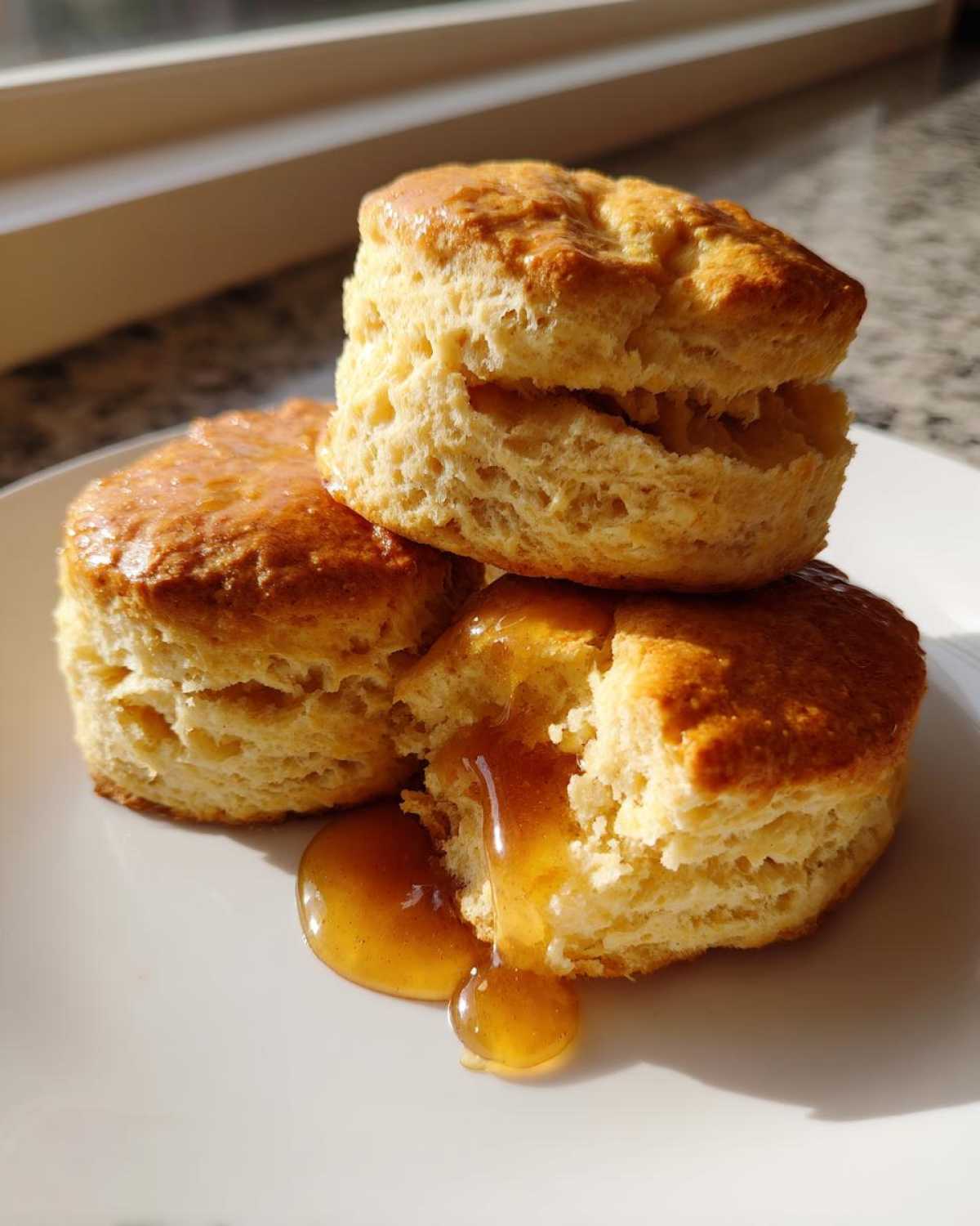 Three fluffy sweet potato biscuits stacked on a white plate with honey dripping down the side.