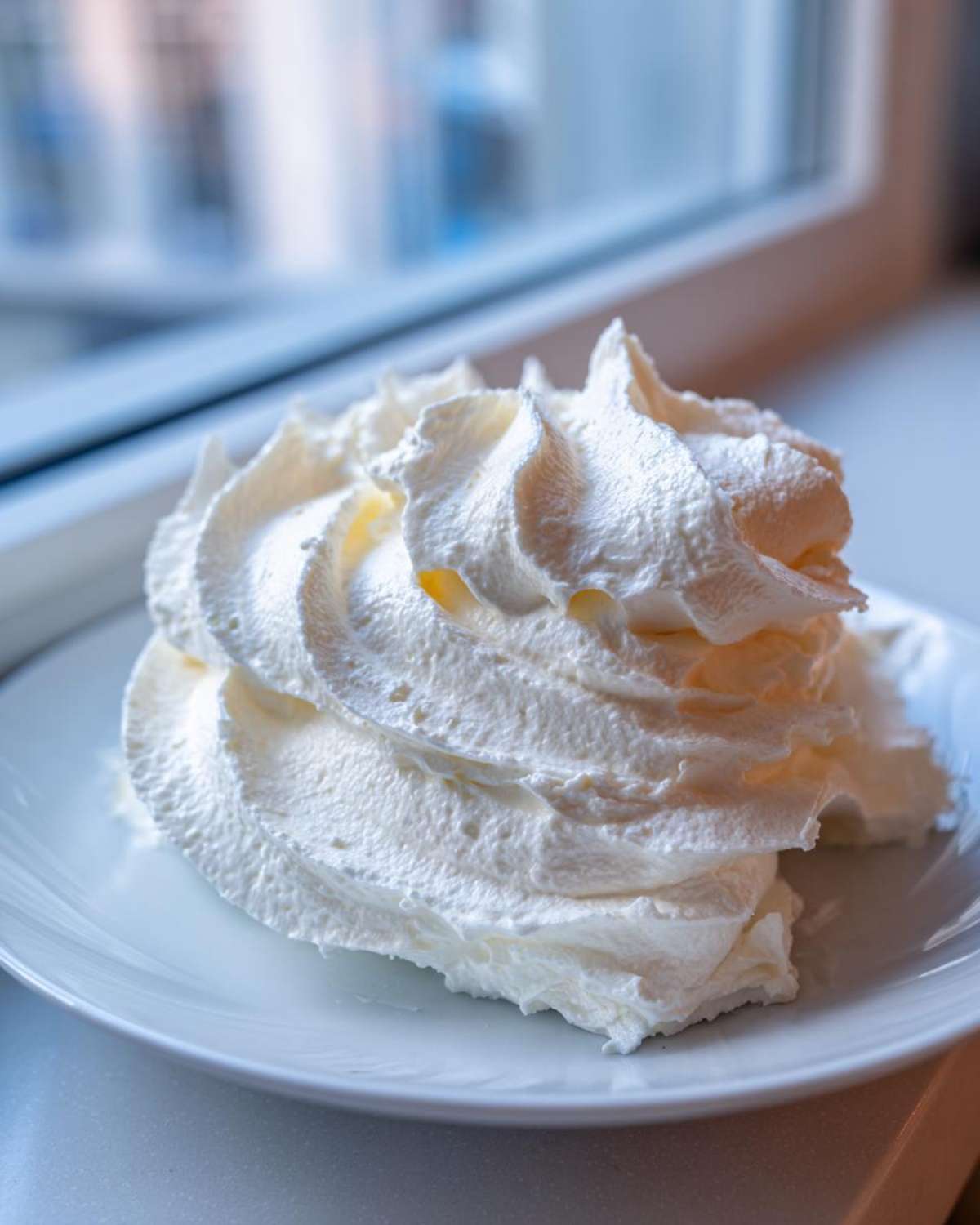 A swirl of fluffy white whipped topping, similar in texture to cream cheese frosting, served on a white plate.