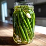 A glass jar filled with fresh green beans, dill, garlic, and mustard seeds for making dilly beans.