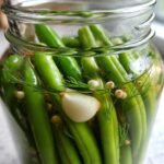 Close-up of fresh green beans packed tightly in a glass jar with dill, peppercorns, and garlic for making dilly beans.