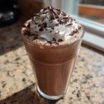 A tall glass filled with rich, blended frozen hot chocolate, topped with whipped cream and chocolate shavings.