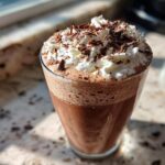 A tall glass of rich frozen hot chocolate topped with whipped cream and chocolate shavings.