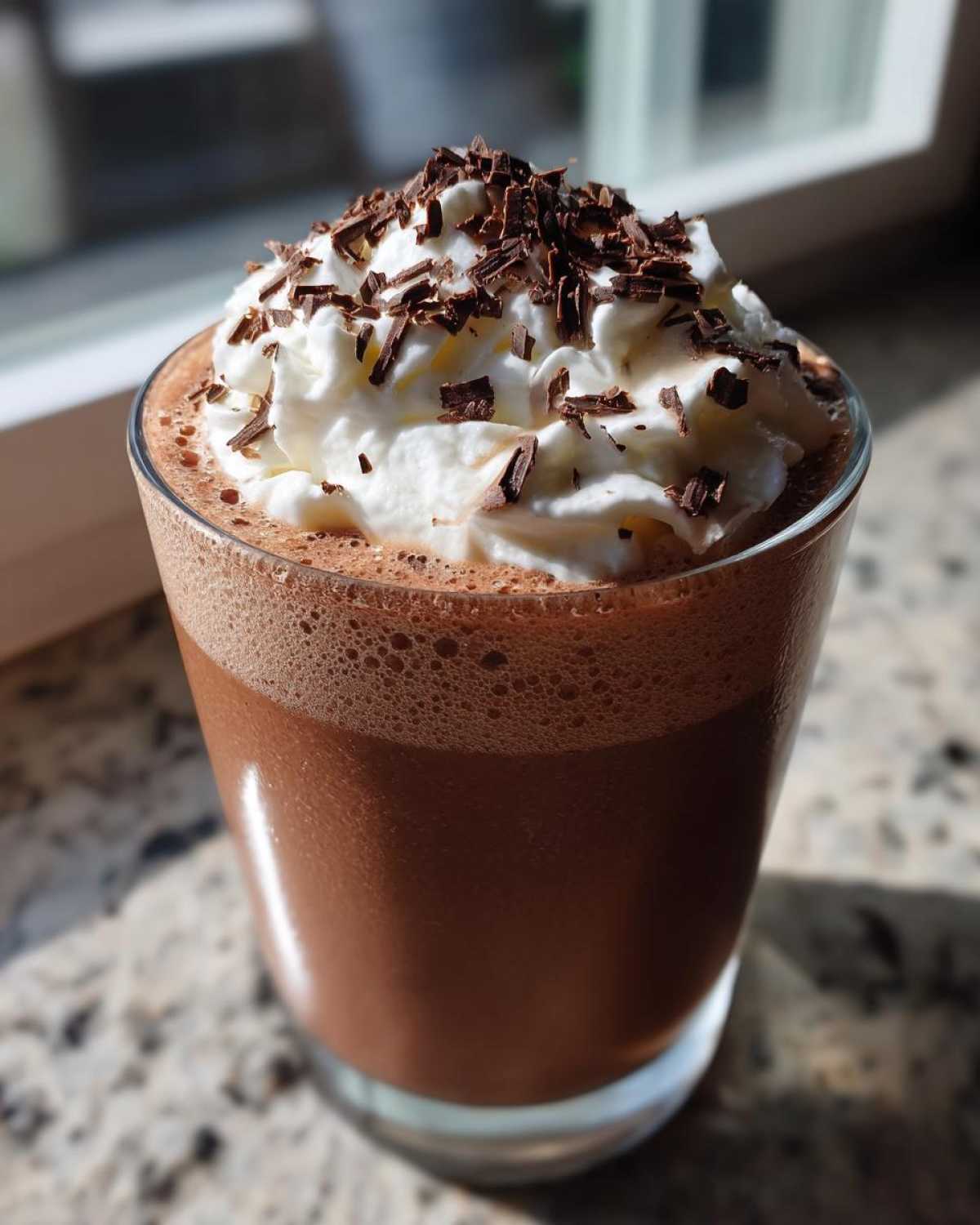 A tall glass of rich frozen hot chocolate topped with whipped cream and chocolate shavings.