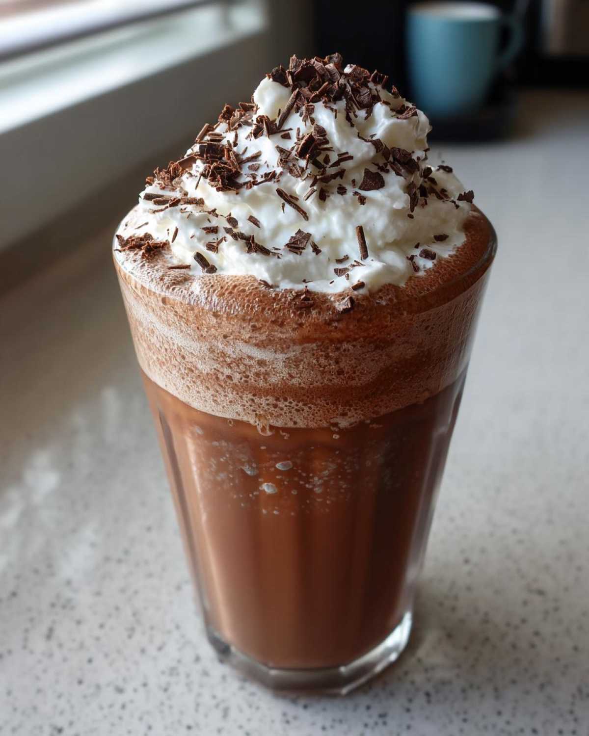 A tall glass filled with rich, blended frozen hot chocolate topped with whipped cream and chocolate shavings.