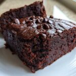 Close-up of two fudgy black bean brownies stacked slightly, topped with chocolate chips on a white plate.