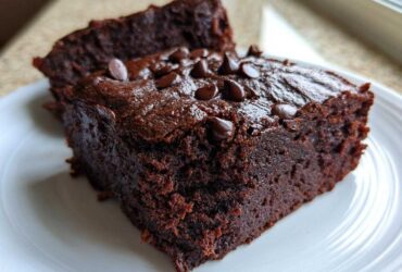 Close-up of two fudgy black bean brownies stacked slightly, topped with chocolate chips on a white plate.