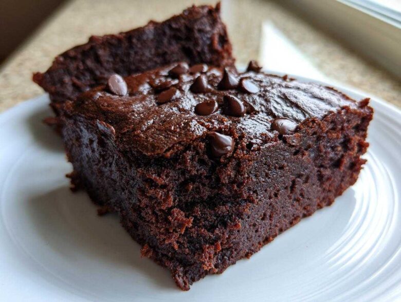 Close-up of two fudgy black bean brownies stacked slightly, topped with chocolate chips on a white plate.