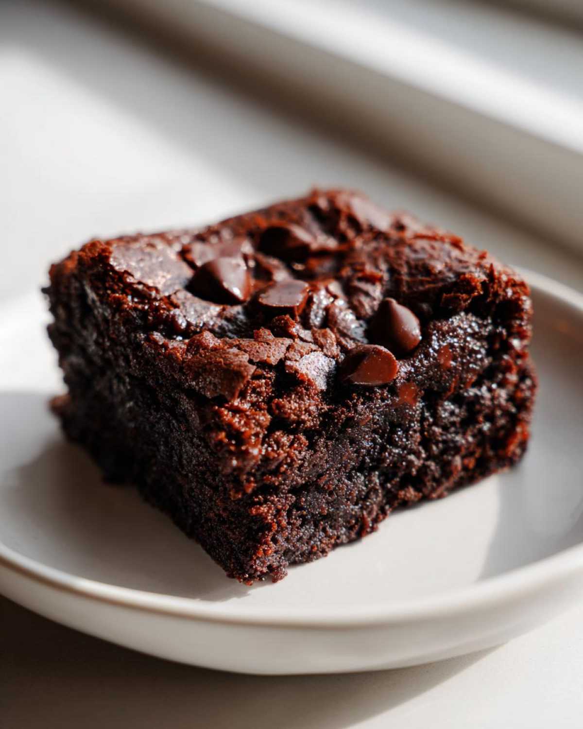 Close-up of a single, fudgy square of black bean brownies topped with melted chocolate chips.