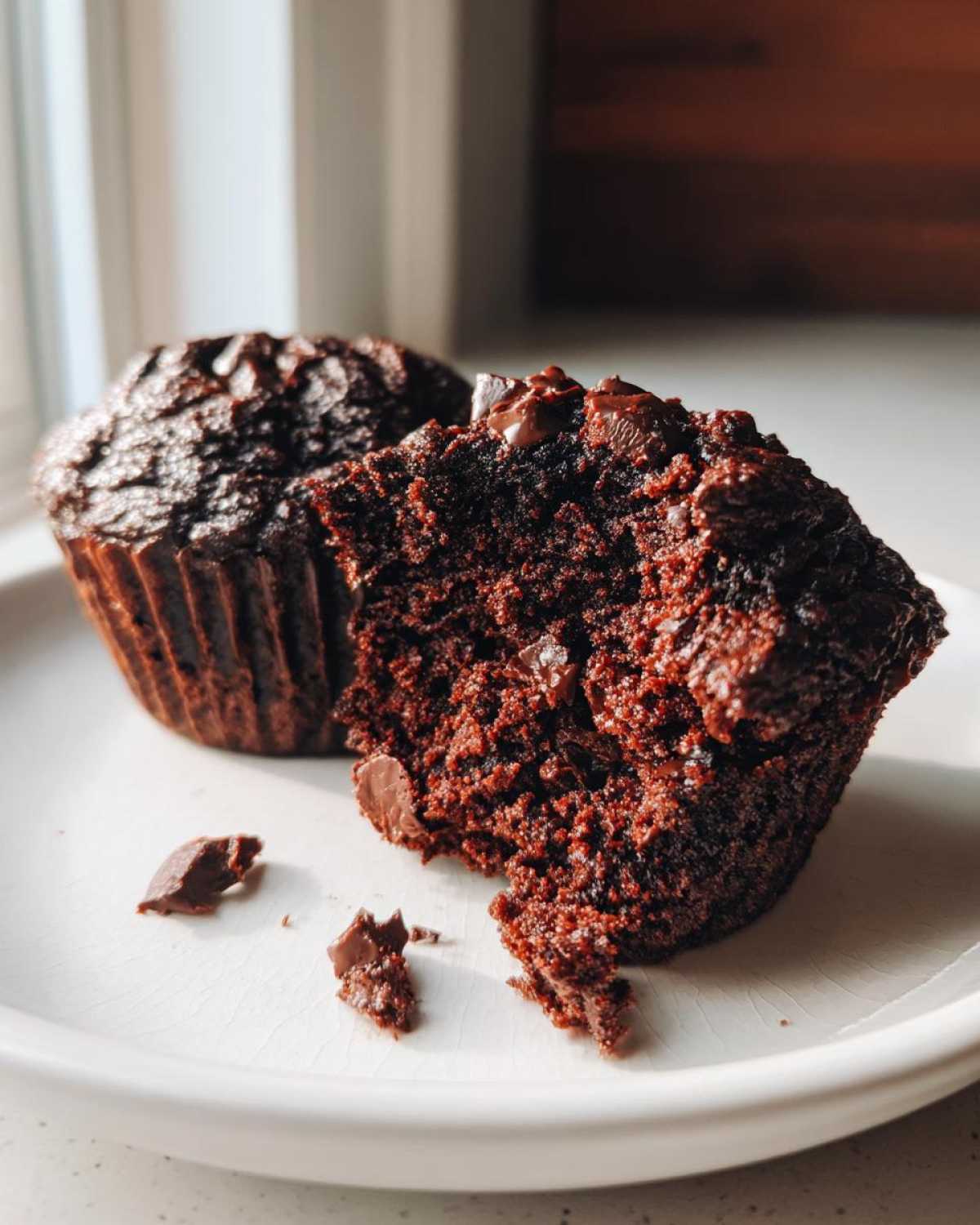 Close-up of a fudgy chocolate zucchini muffin broken in half, showing moist texture and chocolate chips.