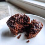 Close-up of a fudgy chocolate zucchini muffin broken in half, showing the moist interior and chocolate chips.