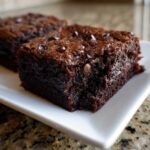 Close-up of a fudgy square of date brownies topped with melted chocolate chips on a white plate.