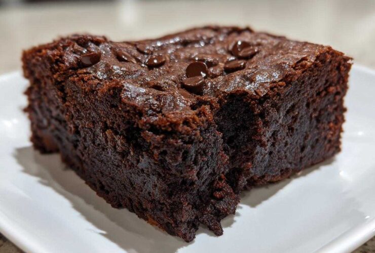 Close-up of a rich, fudgy slice of date brownies topped with chocolate chips on a white plate.