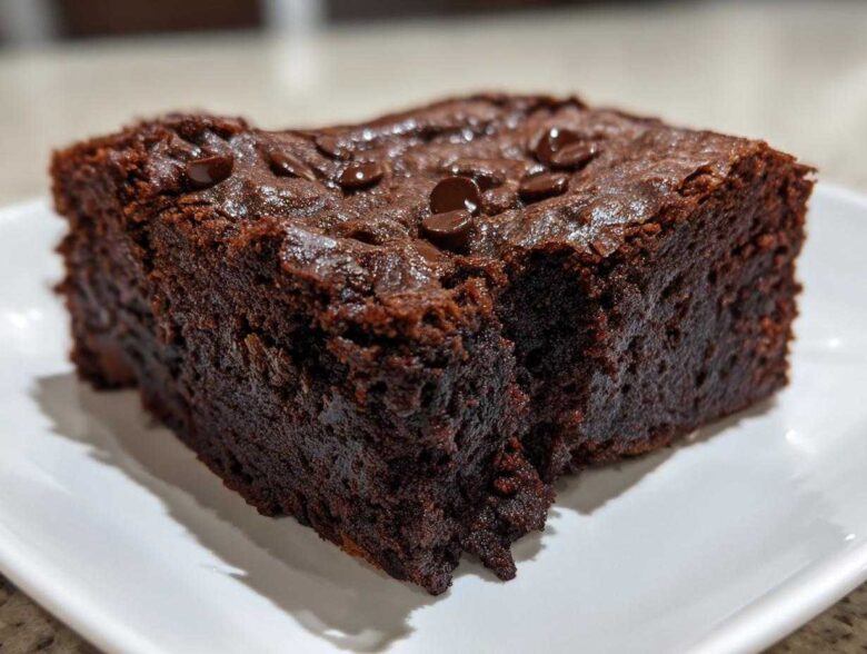 Close-up of a rich, fudgy slice of date brownies topped with chocolate chips on a white plate.