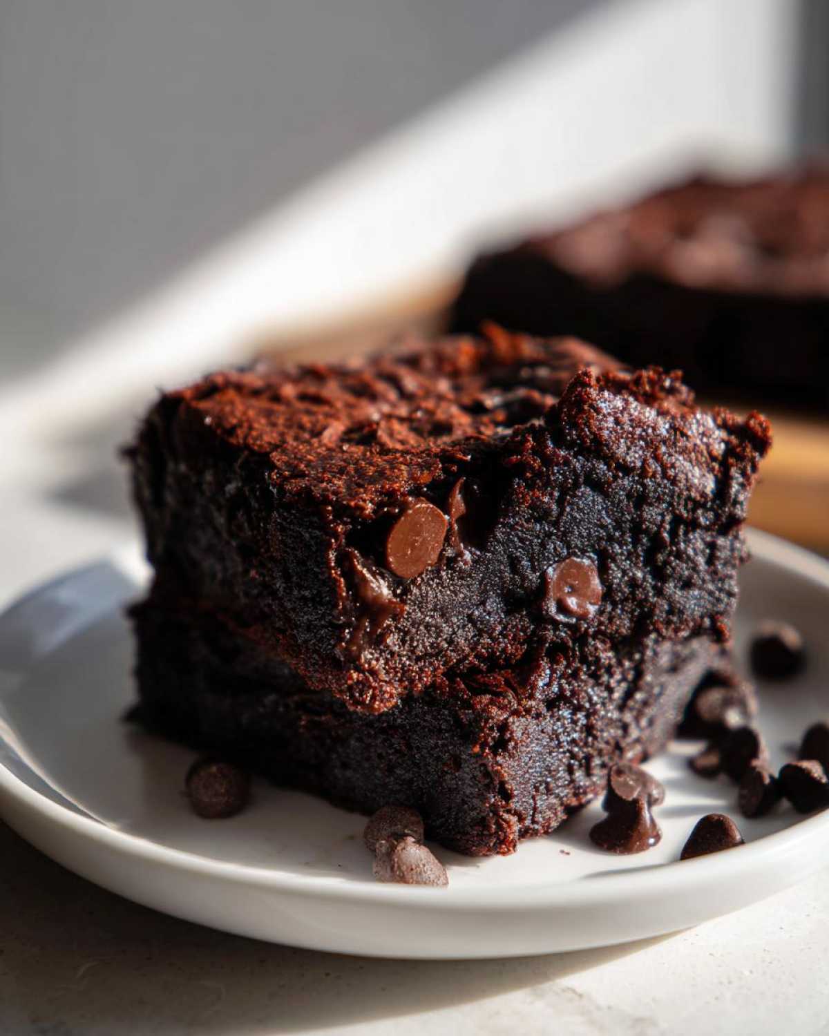 Close-up of a fudgy square of date brownies topped with melted chocolate chips on a white plate.
