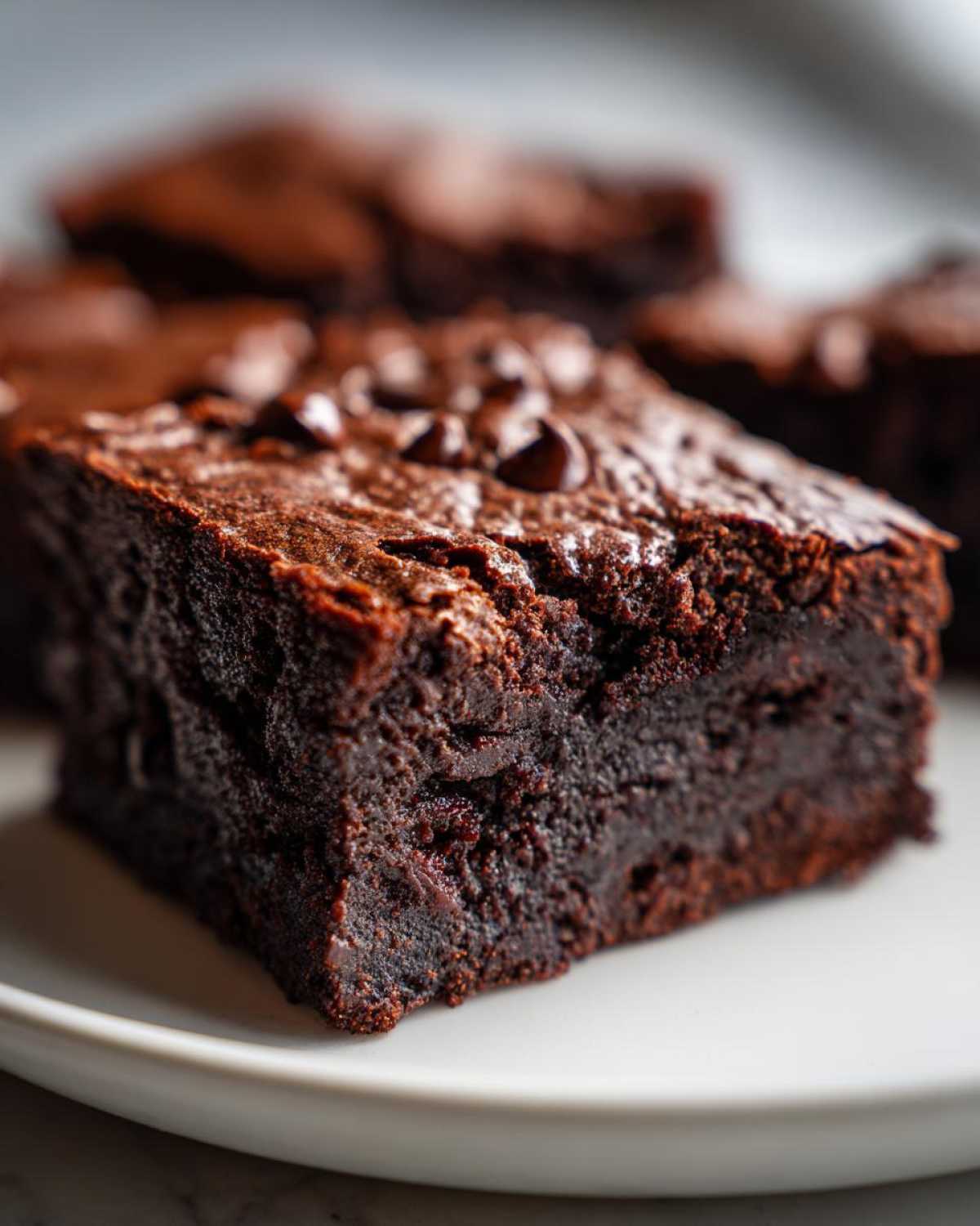 A close-up, rich, dark square of fudgy sweet potato brownies topped with chocolate chips on a white plate.