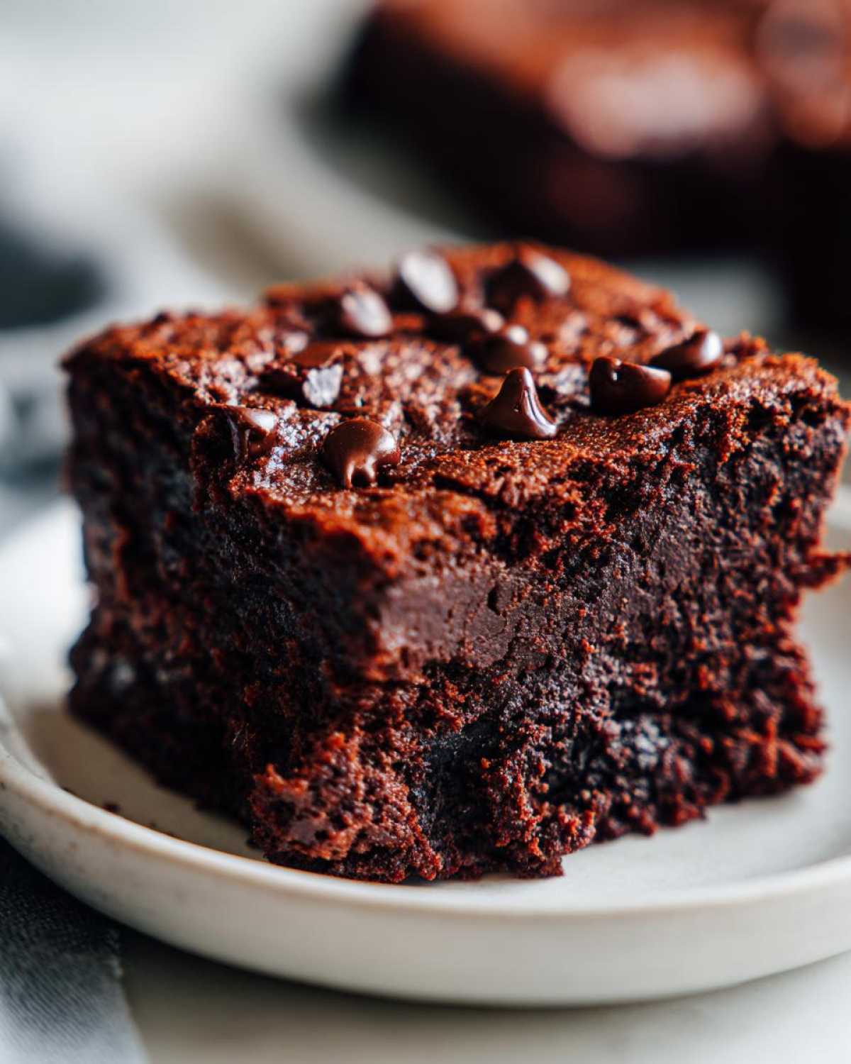 Close-up of a fudgy square of sweet potato brownies topped with melted chocolate chips on a white plate.