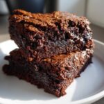 Two stacked, fudgy sweet potato brownies with visible chocolate chips on a white plate.