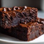 Close-up of two stacked, fudgy sweet potato brownies topped with melted chocolate chips on a white plate.