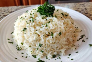 A mound of fluffy white garlic butter rice garnished with chopped parsley on a white plate.