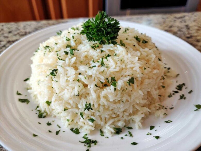 A mound of fluffy white garlic butter rice garnished with chopped parsley on a white plate.