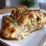 Close-up of a juicy Garlic parmesan chicken bake breast, showing the white interior and golden, cheesy topping.
